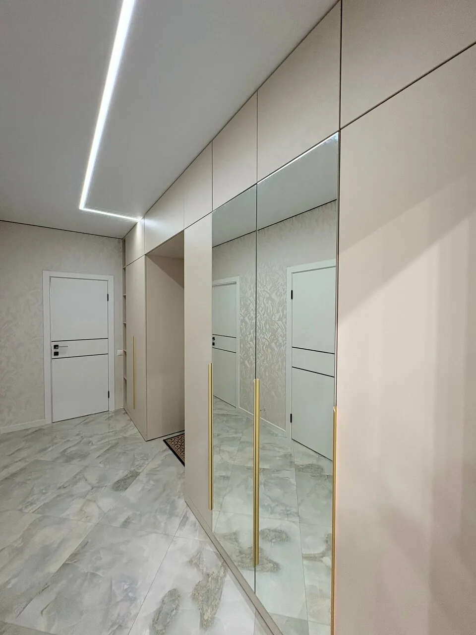 Бежевый шкаф в прихожей во всю стену с зеркальными дверями и вертикальными латунными профилями