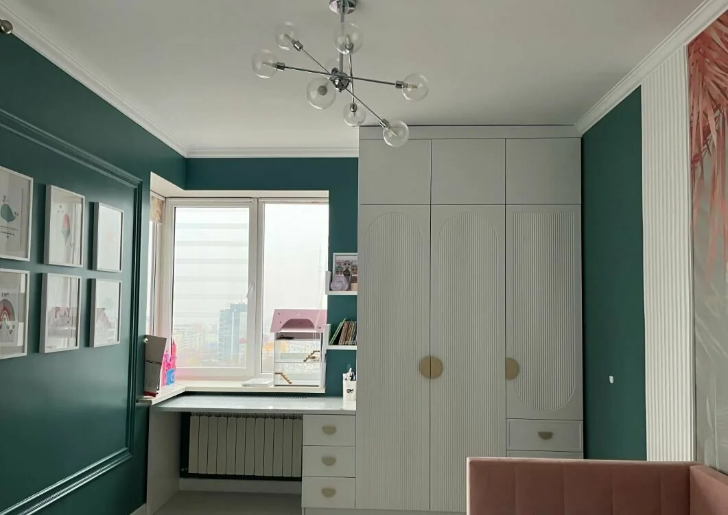 Белый шкаф под потолок с фрезерованными фасадами и письменным столом у окна в детской